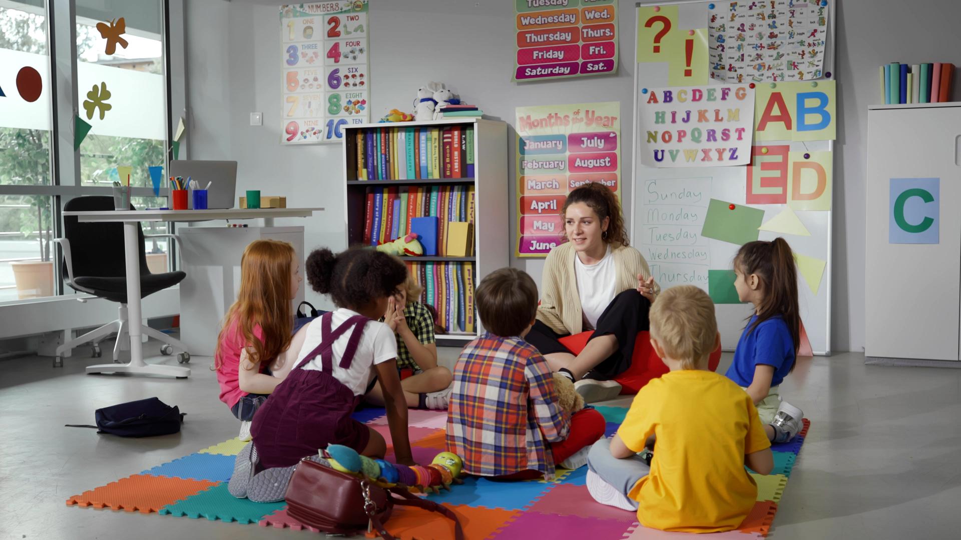 Small nursery school children with teacher sitting on floor having lesson